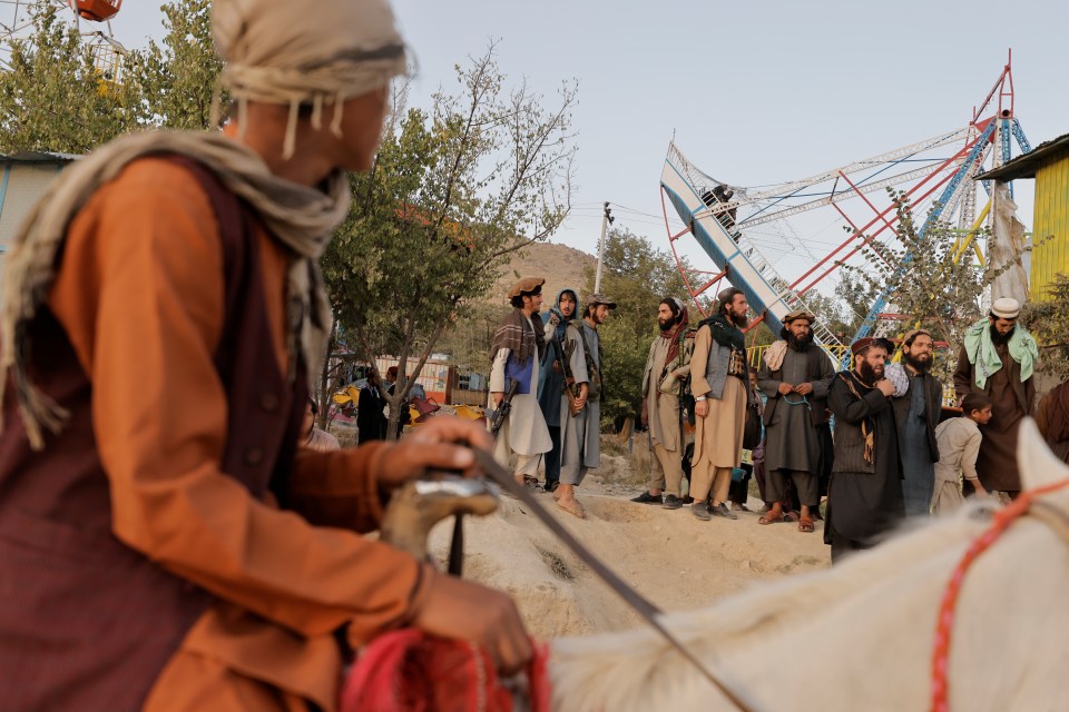 Taliban fighter riding a horse watches others riding a swinging pirate ship