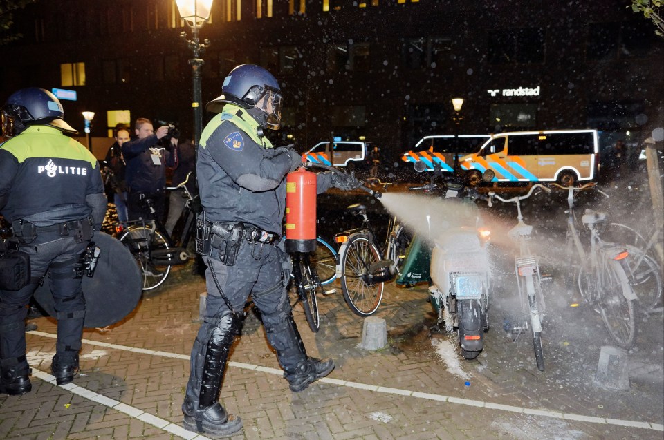 An anti-riot police officer extinguishes a burning scooter