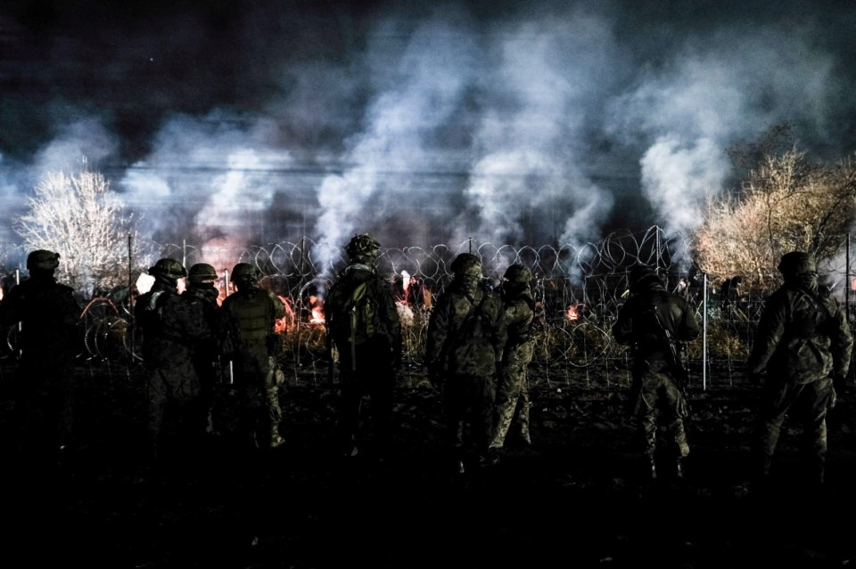 Polish guards near a barbed wire fence on the frontier as hundreds of migrants gather on the Belarusian side