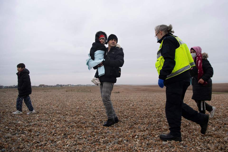 A man holds a child as migrants walk along the beach after being helped ashore