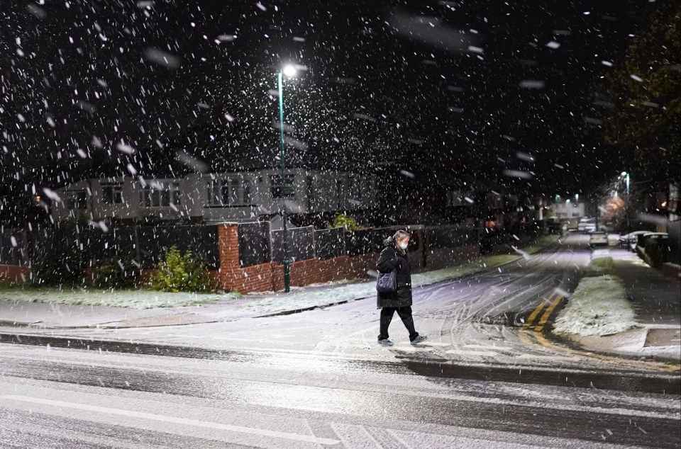 A woman crosses a snow covered road during a heavy snow shower in Saltburn By The Sea