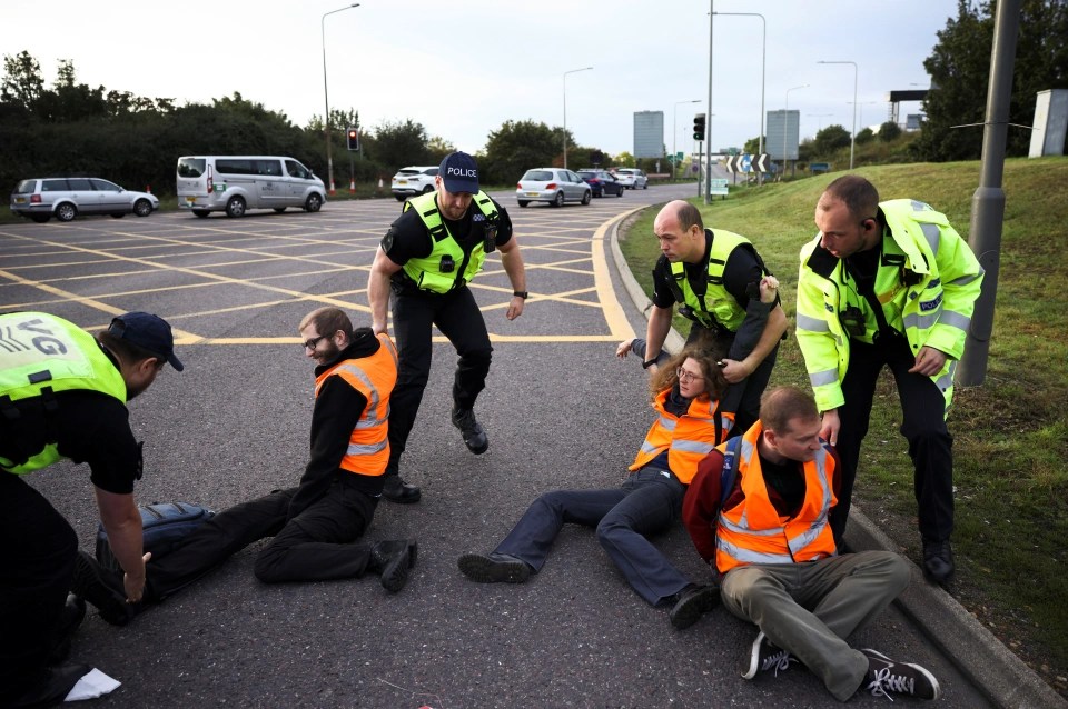 Police officers remove Insulate Britain activists as they block a roundabout