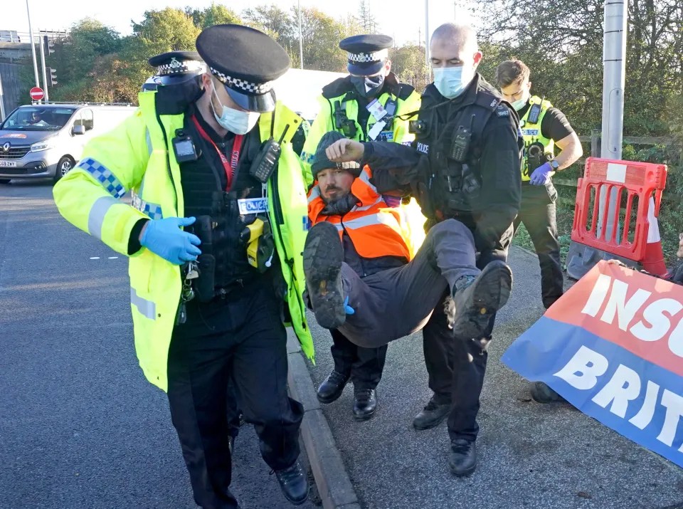 Police officers detain a protester at an Insulate Britain roadblock near to the the South Mimms roundabout at the junction of the M25 and A1