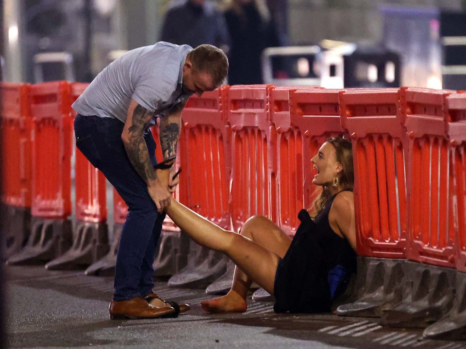 A couple laugh while trying to get her shoes off after a Leeds night out