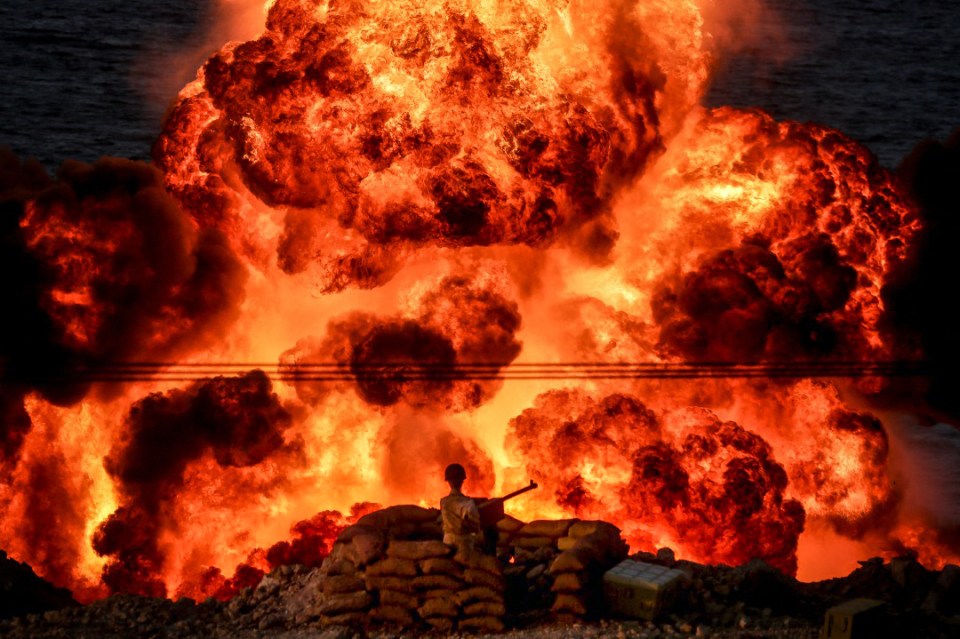 An Iranian soldier looks on as a wall of flame shoots up from a missile target