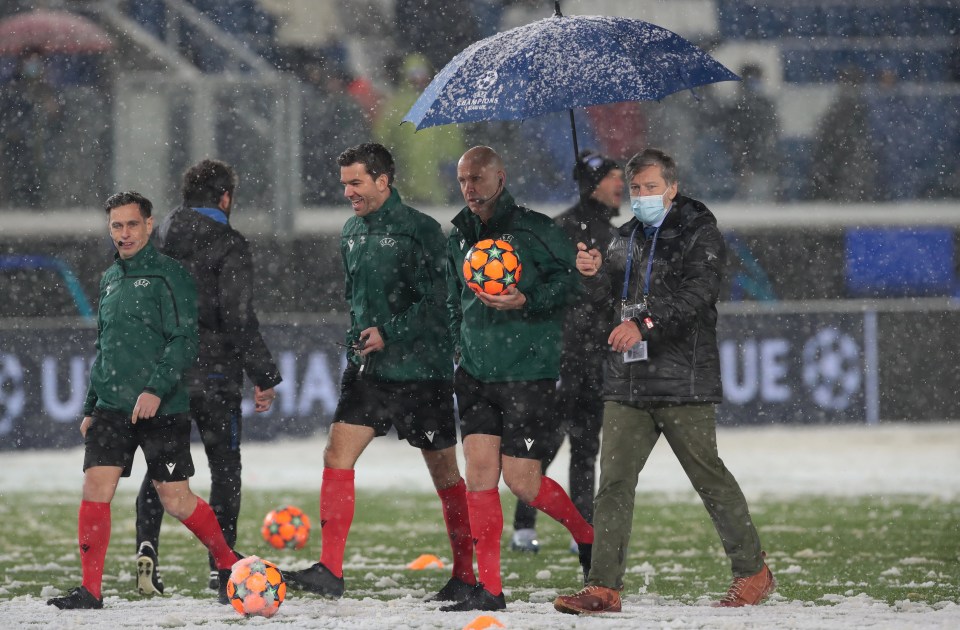 Referee Anthony Taylor inspects the pitch in Northern Italy under an umbrella