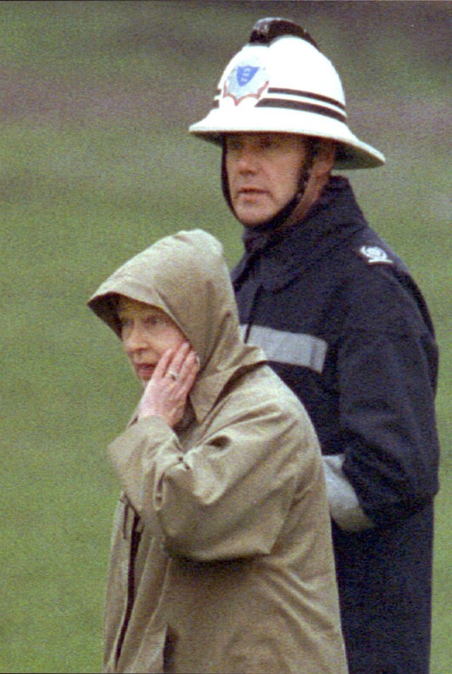 The monarch holds her hand to her face as a fireman escorts her around the grounds of the fire-damaged Windsor Castle