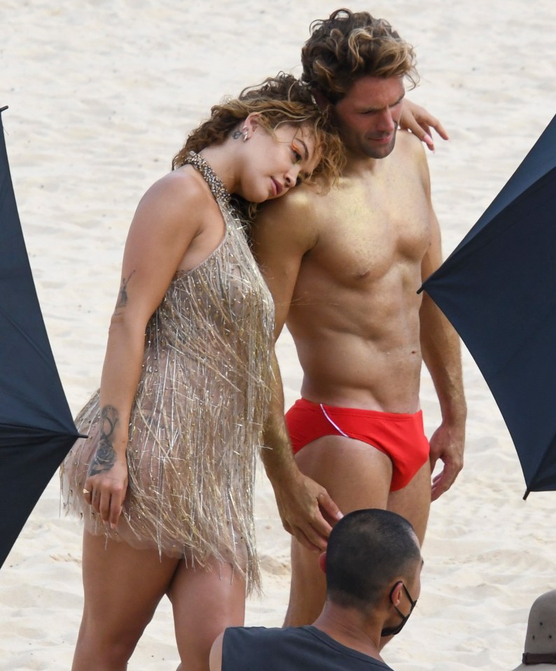 Rita Ora looked in her element as she draped herself over a group of buff Speedo-clad guys on a Sydney beach in Australia