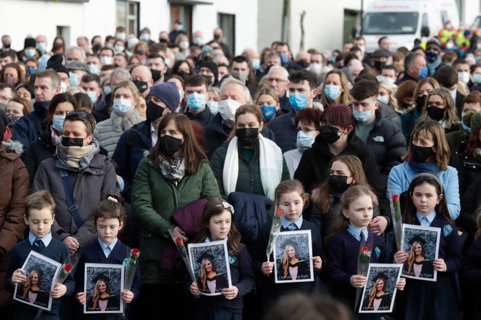 Pupils from Ashling Murphy's class hold photographs of her and red roses outside St Brigid's Church, Mountbolus