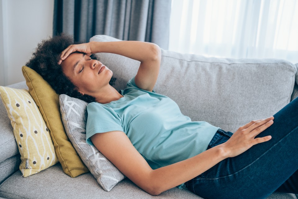 Woman lying on couch holding her head.