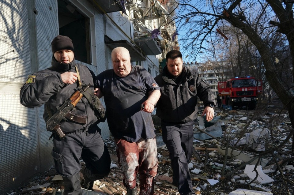 Ukrainian security forces accompany a wounded man after an airstrike hit an apartment complex in Chuhuiv