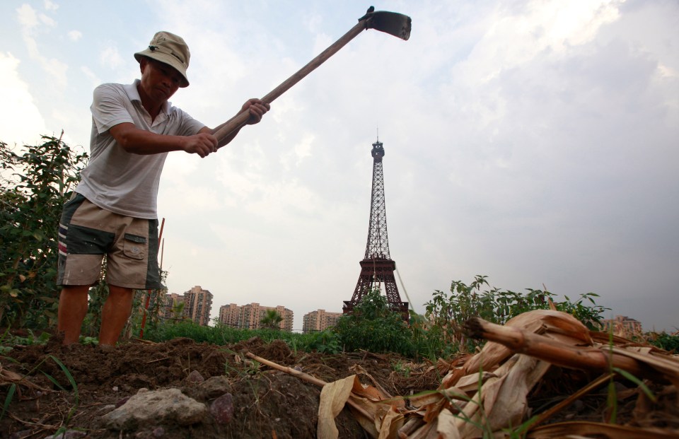 A farmer tills the field near the replica of the Eiffel Tower at the Tianducheng development in Hangzhou