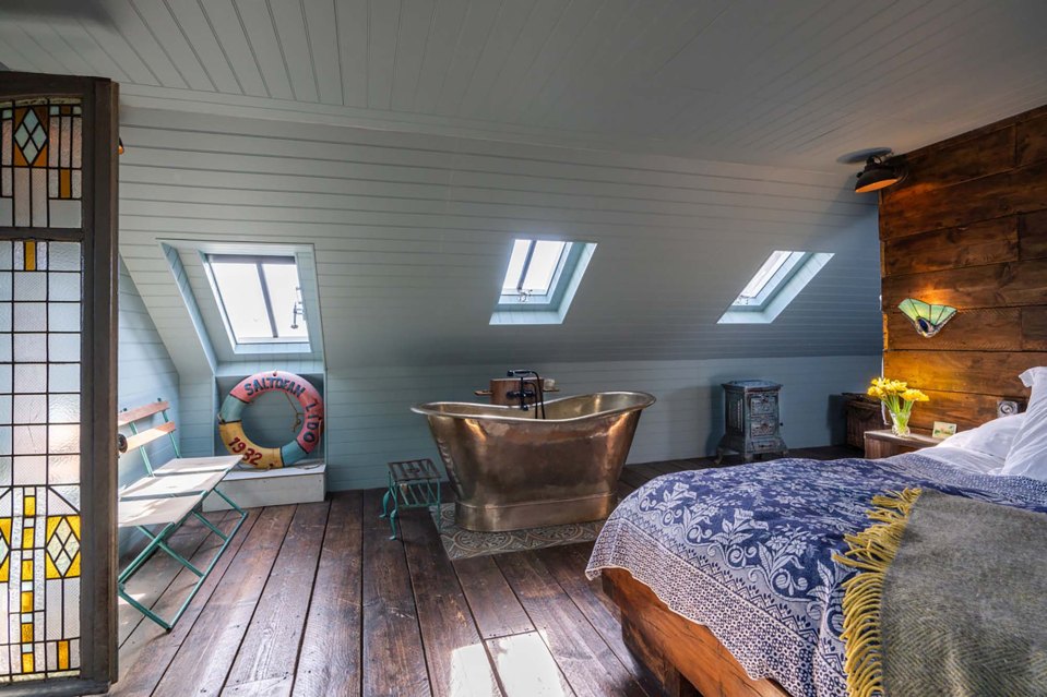 An ocean-themed bedroom features a brass bathtub and wooden decked floor