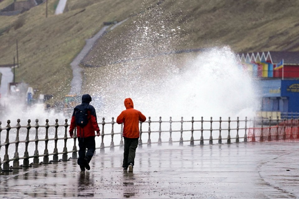 Big waves hit the sea wall at Whitby Yorkshire as people walk along the beach path