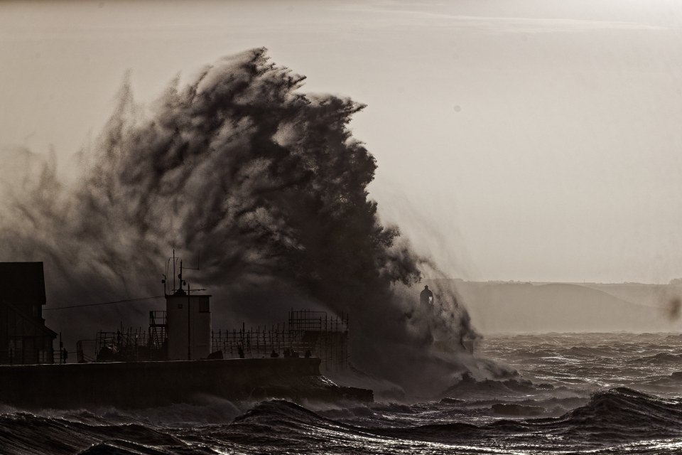 Waves batter the promenade wall and the lighthouse in Porthcawl, Wales