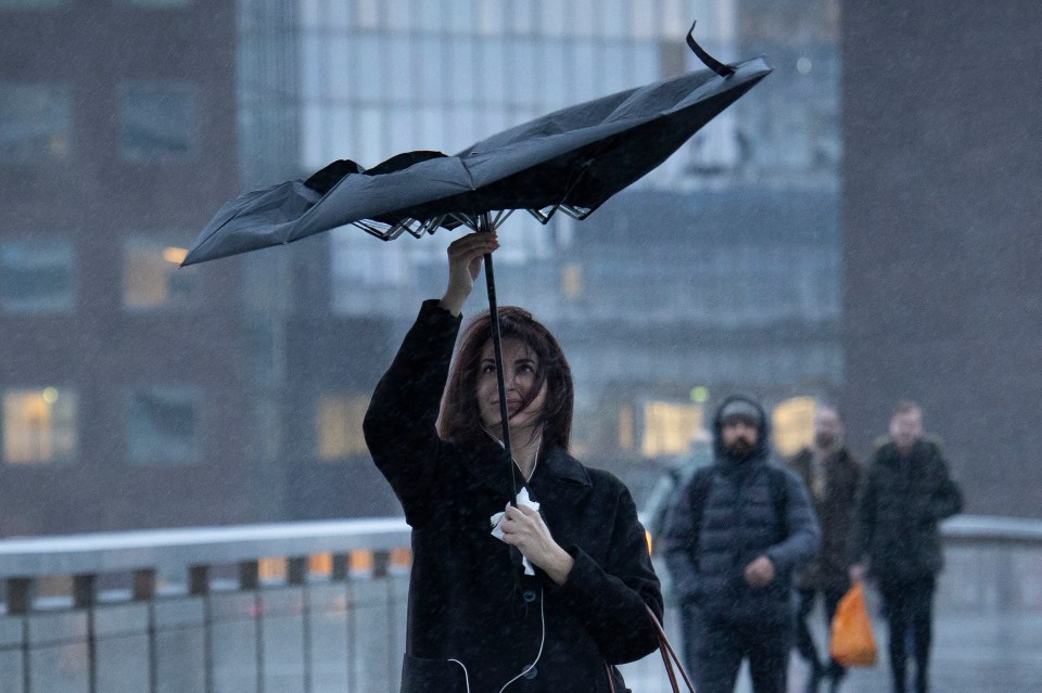 A commuter struggles with her umbrella as she crosses London Bridge