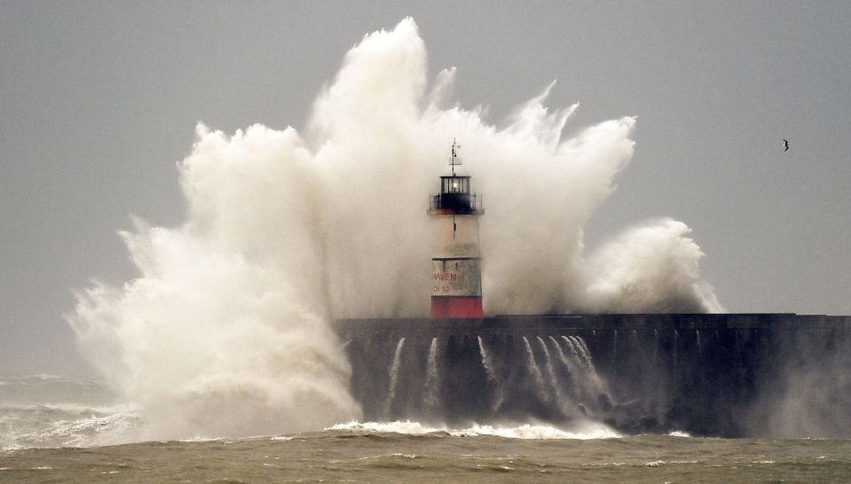 Waves crash over Newhaven Lighthouse and the harbour wall