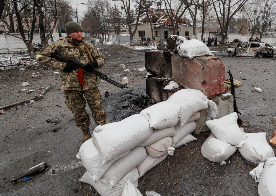 Ukrainian soldiers stand in the aftermath of an overnight shelling at the Ukrainian checkpoint near Kyiv