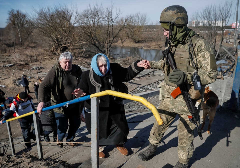 A member of the Ukrainian forces helps a woman to cross the Irpin river as she evacuates