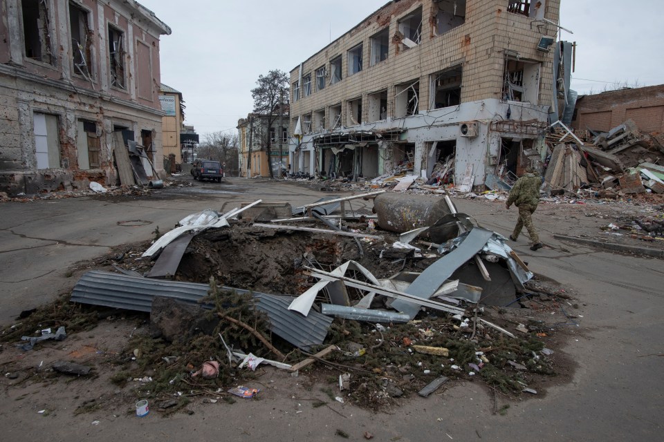 A Ukrainian service member walks past a bomb crater in Okhtyrka, in the Sumy region