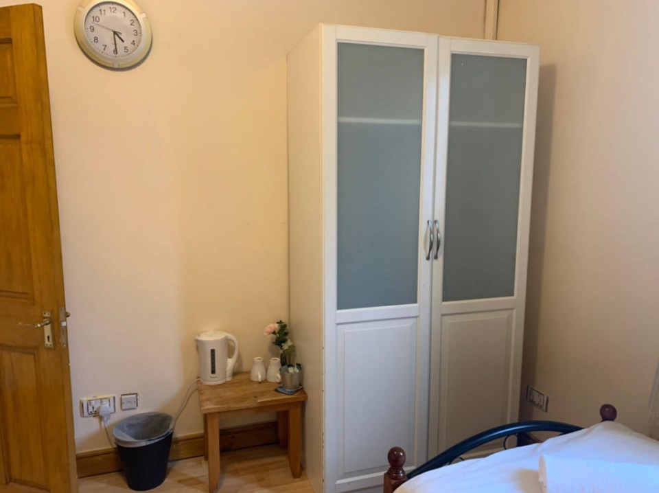 The room features a wardrobe and small side table with a kettle and two mugs