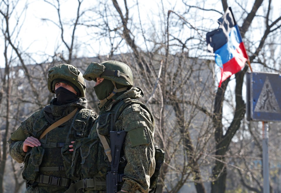 Service members of pro-Russian troops stand guard as evacuees board buses to leave the Mariupol