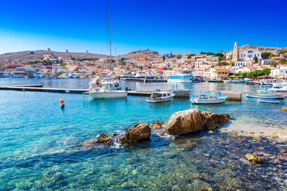 On the small island of Halki, pastel coloured houses line a crescent shaped bay