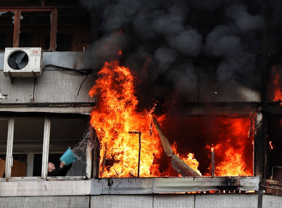 A neighbour uses a bucket of water on 12ft flames in a futile bid to extinguish the fire