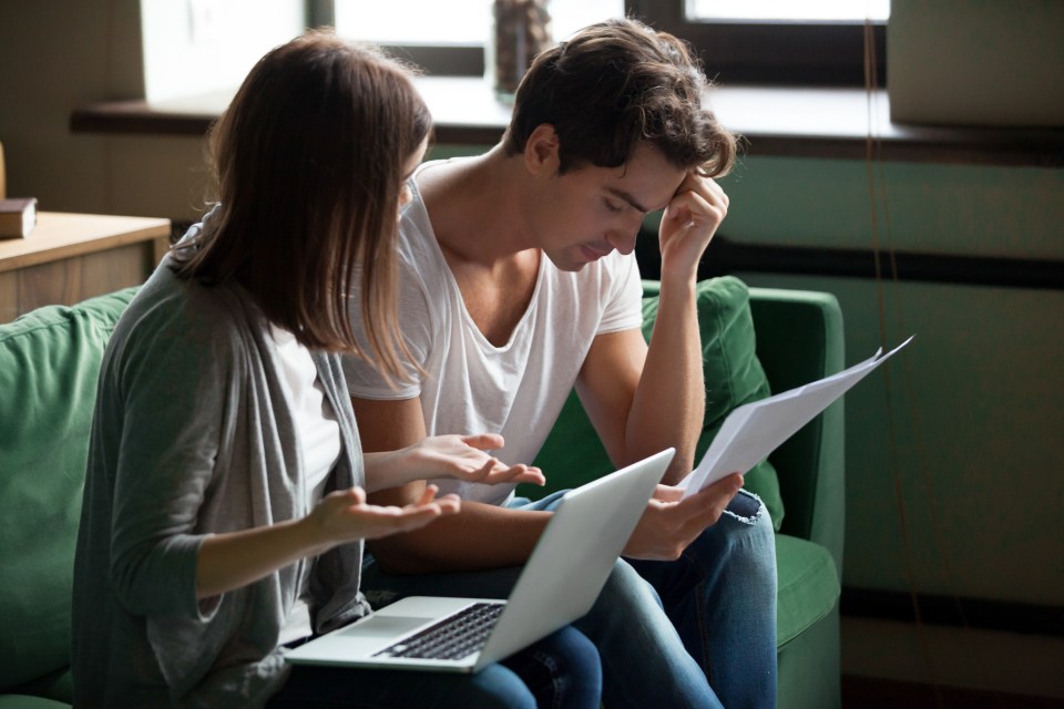 Millennial stressed young couple sitting on sofa at home and checking unpaid bills, taxes, due debt, bank account balance. Bankruptcy, debt and lack of money, financial problems in family concept