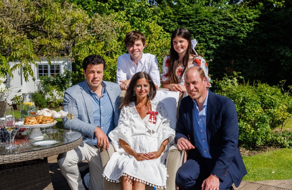 Deborah. surrounded by her family, receives her Damehood from Prince William in her garden