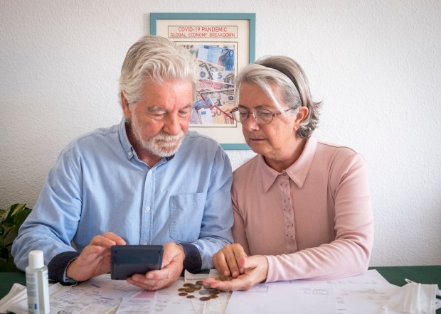 an elderly couple looking at their finances in front of a framed picture that says covid-19 pandemic global economy breakdown