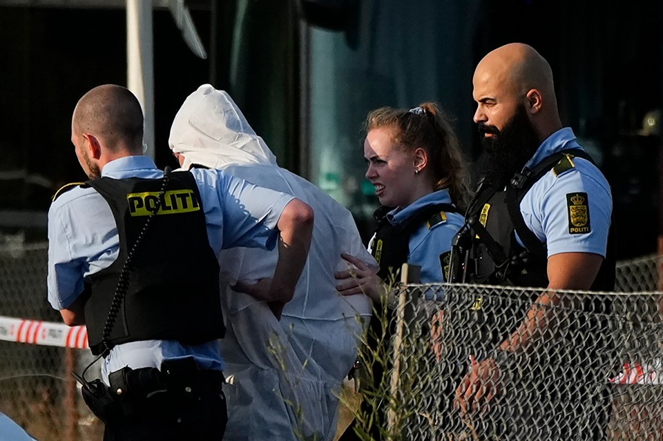 Police lead away figure in a white bodysuit after the massacre