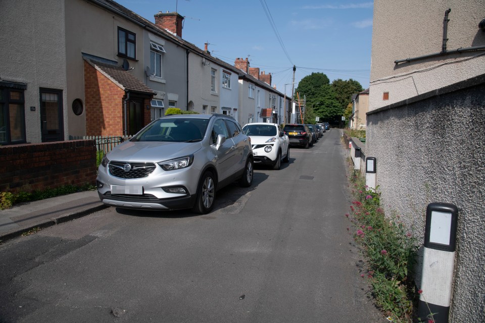 Cars can be seen parked along the narrow street, with no road markings