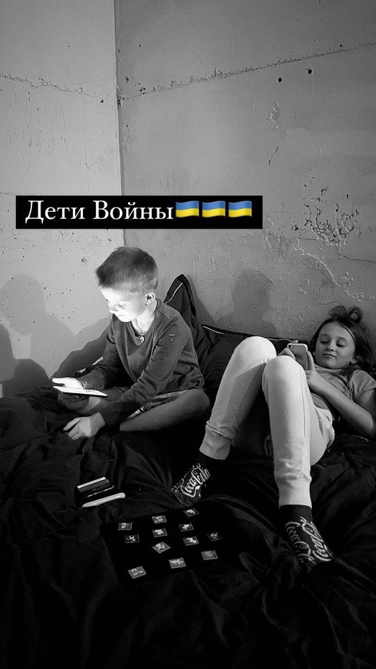 Two children, a boy and a girl, lie on a bed using electronic devices.  The text "Дети Войны" (Children of War) and Ukrainian flags are visible.