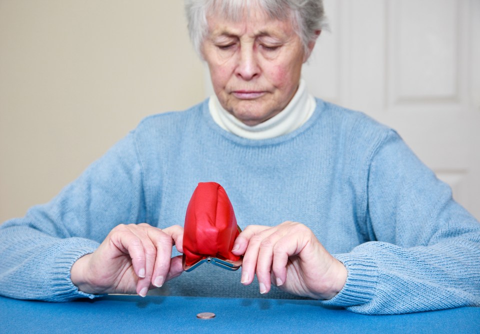 an elderly woman is sitting at a table holding an empty wallet