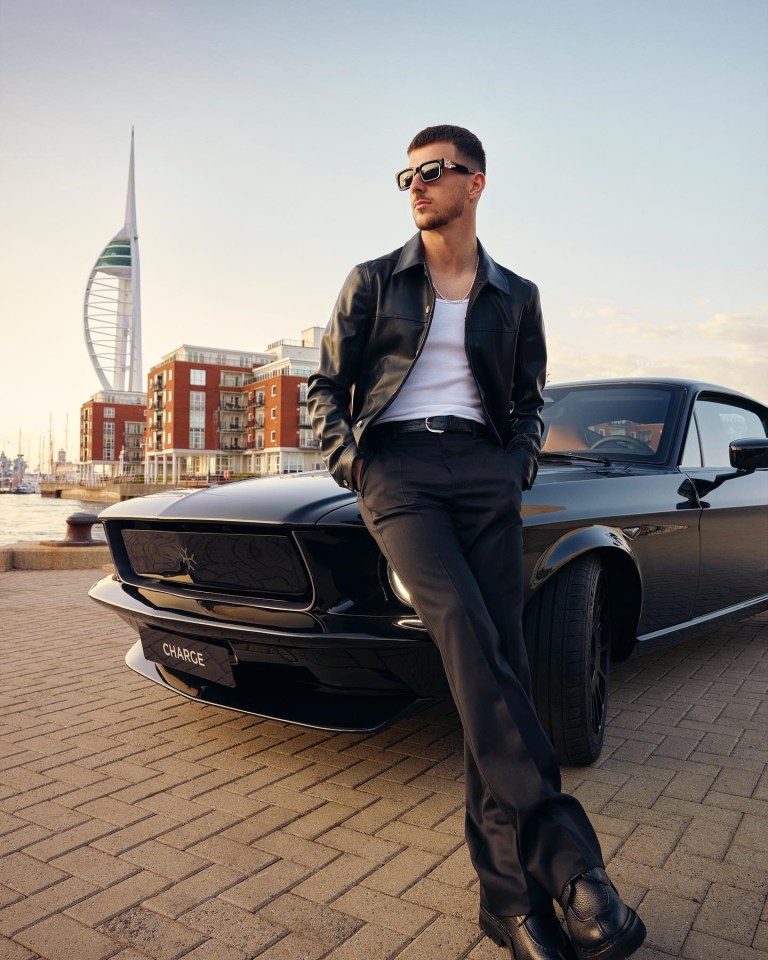 Mount posed in front of a Mustang while wearing a leather jacket and shades