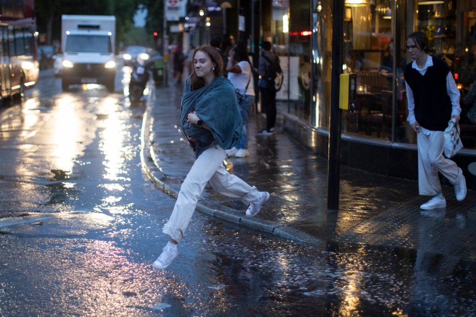 A woman jumped over a puddle as the rain poured in London yesterday