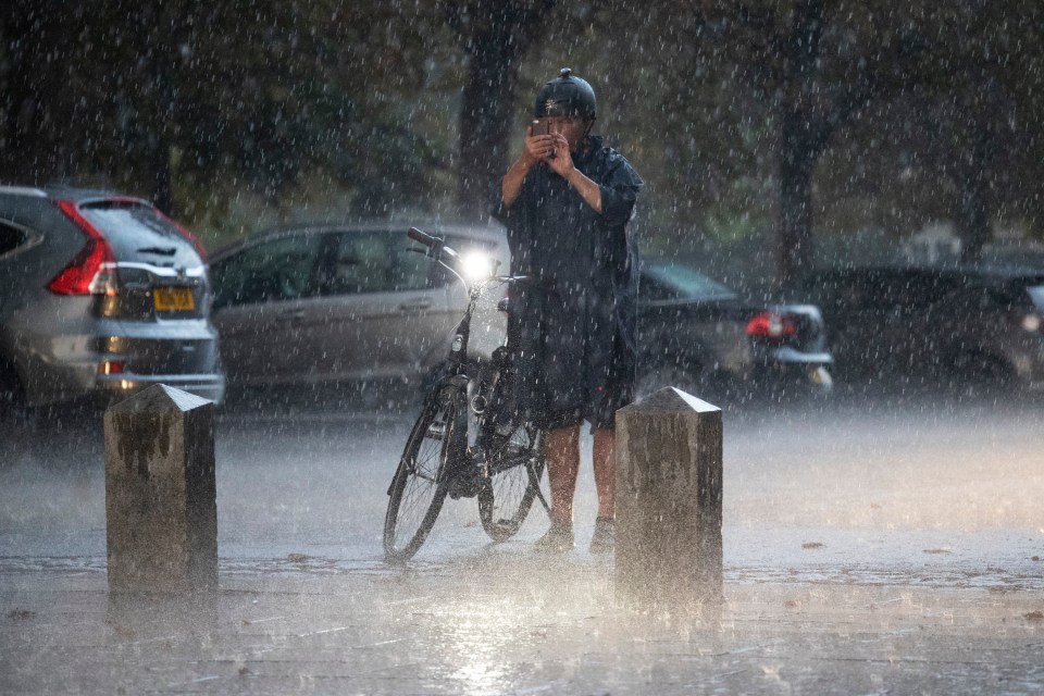 A man attempts to take a picture during heavy rain in Greenwich, London