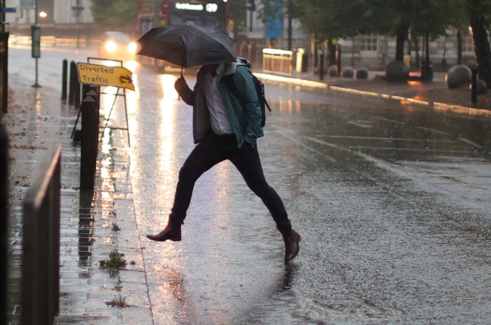 A member of the public jumps over a puddle during heavy rain in Greenwich in South East London