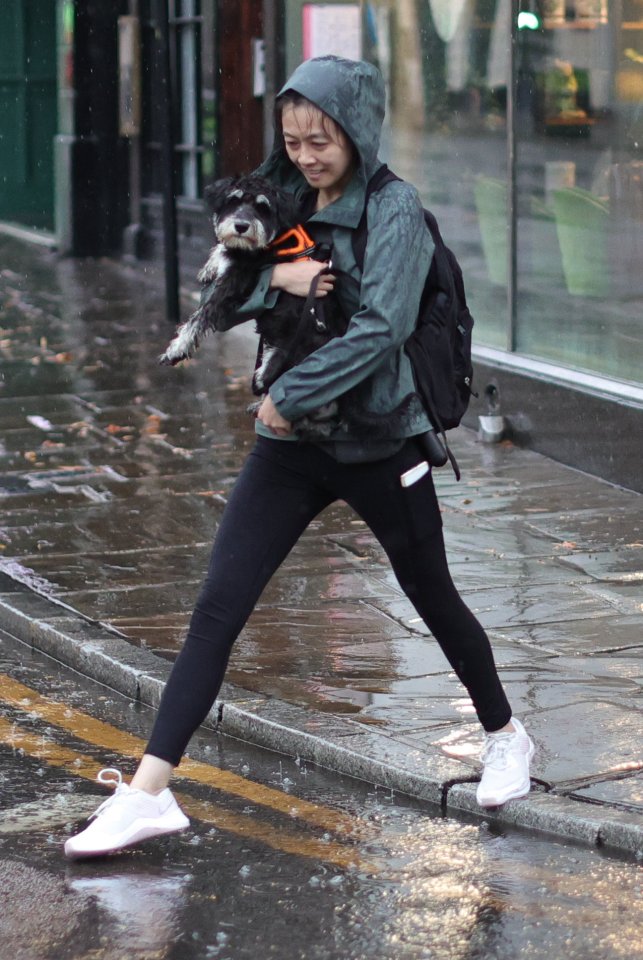 A woman holds her dog as she crosses a puddle during heavy rain in Greenwich, South East London