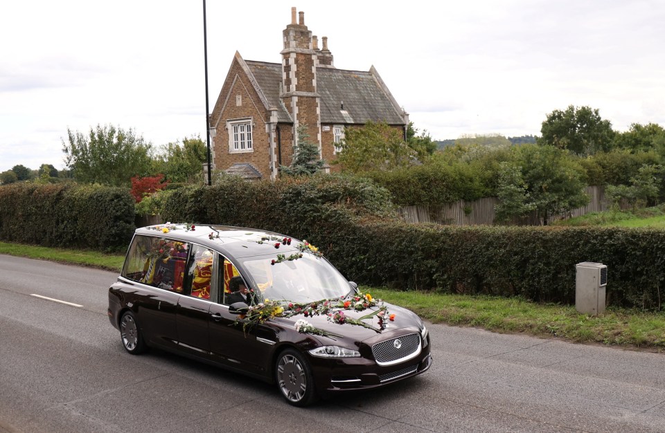 The hearse transporting the coffin, covered in flowers thrown by mourners