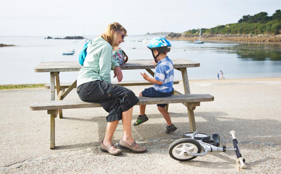 a woman sits on a bench next to a boy wearing a helmet