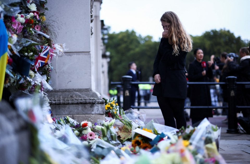 A woman is overcome by emotion as she looks at floral tributes