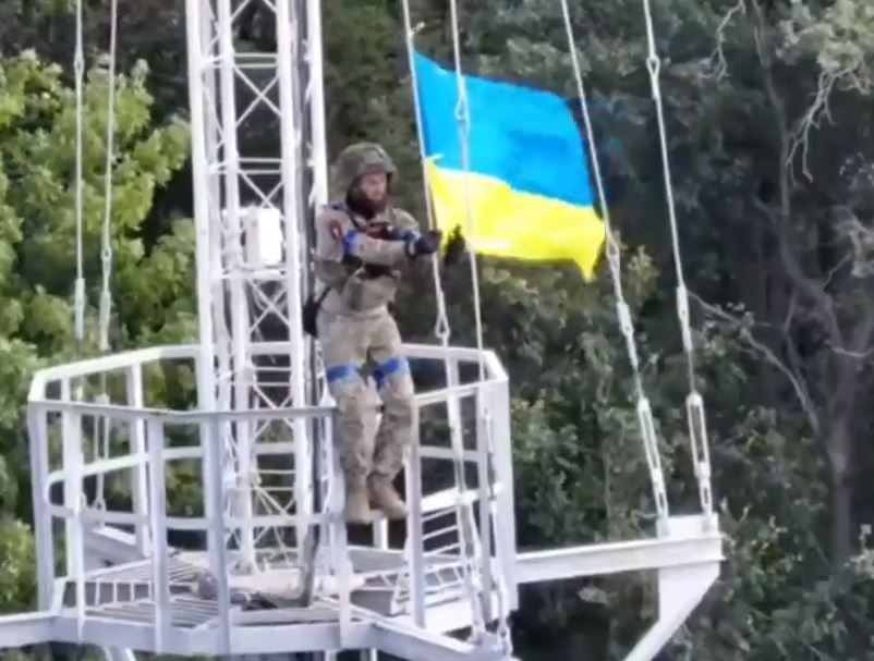 A victorious Ukrainian soldier flying his country's flag from a mast