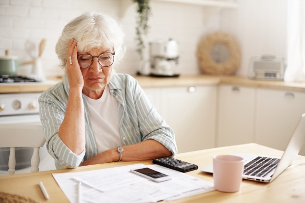 an older woman sits at a table with papers and a laptop