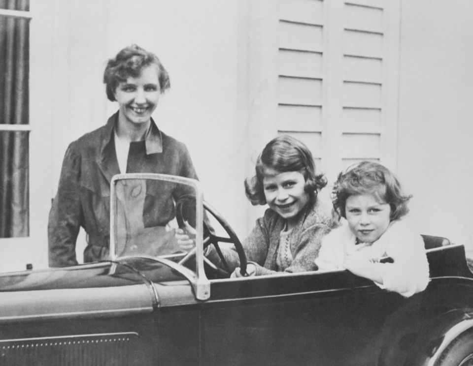 Princess Elizabeth and Princess Margaret play in a miniature automobile while their governess, Marion Crawford, keeps an eye on them