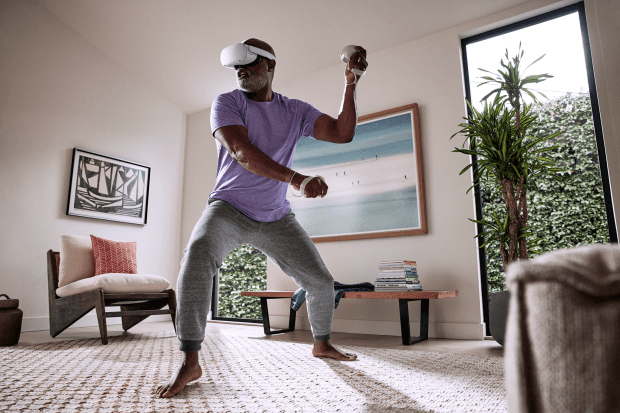 Man using Meta Quest VR headset and controllers while exercising at home.