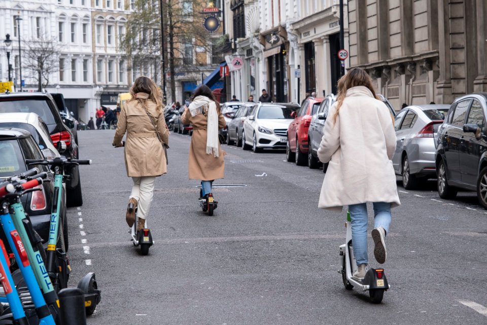 three women are riding scooters down a street with a sign that says 20 on it