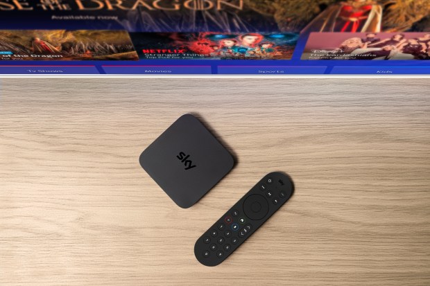 a sky box sits on a wooden table next to a remote control