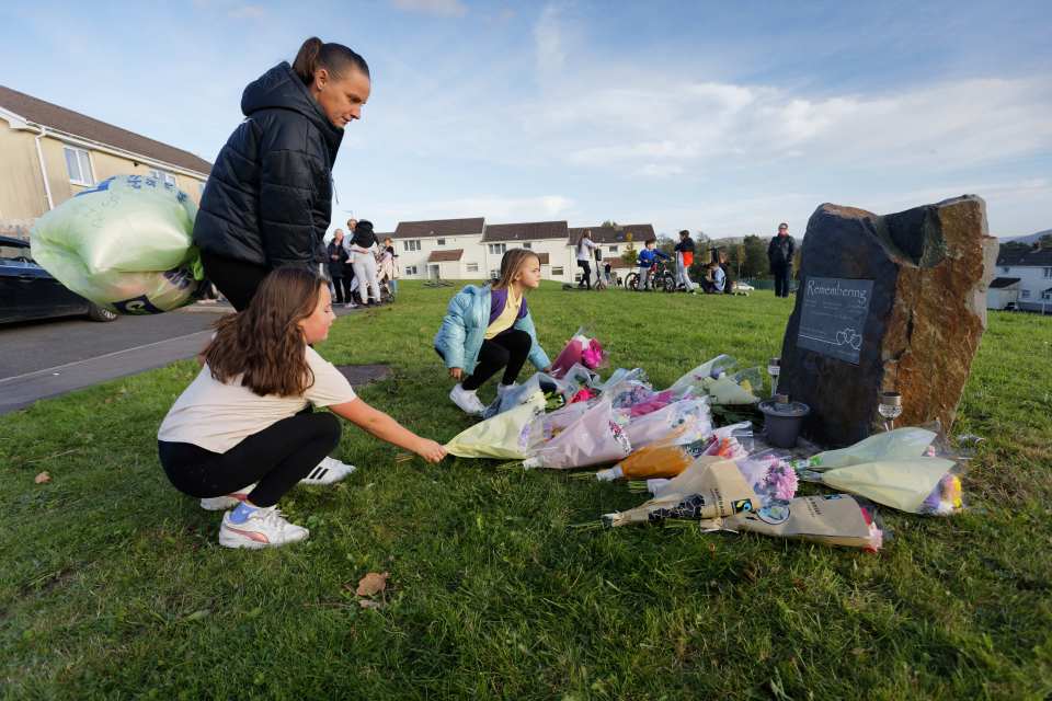 A local woman with two young girls leave flowers by the stone memorial